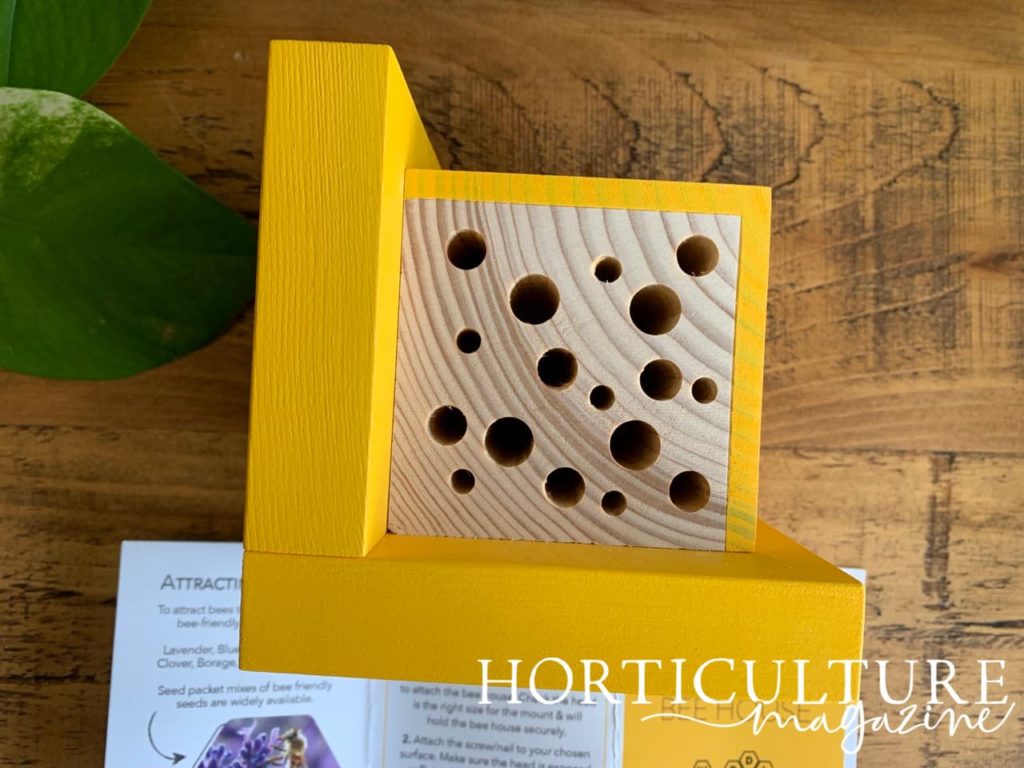 yellow painted wooden bee house with small holes drilled in