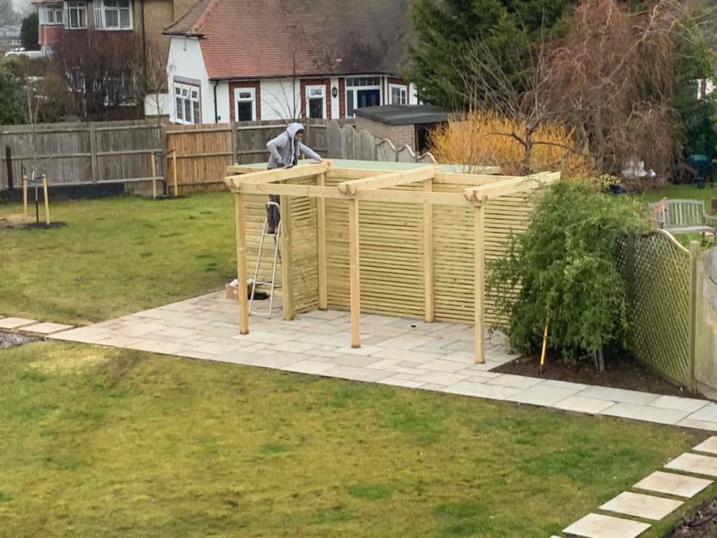 landscape designer on a ladder building a pergola in a large garden
