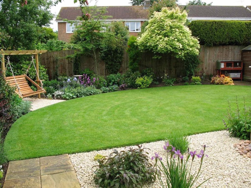 mowed lawn with garden borders surrounding it and a garden swing and patio