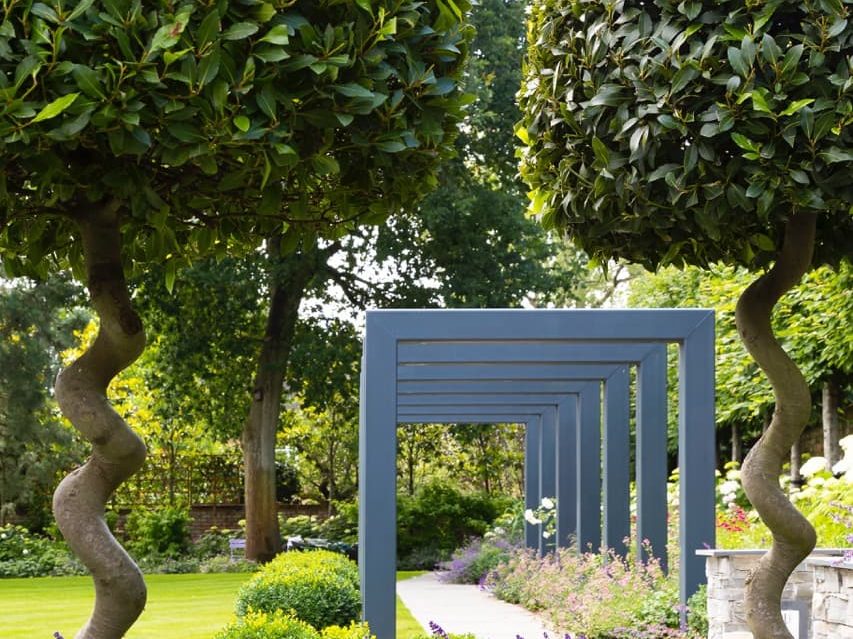 topiary trees and a wooden, blue pergola over a path used in a garden design by Raine Clarke-Wills