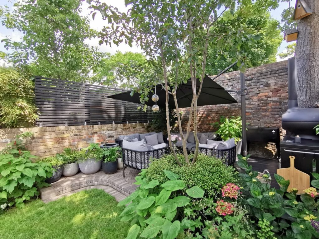 a garden lawn with a sheltered upper patio area with garden borders packed full of green plants