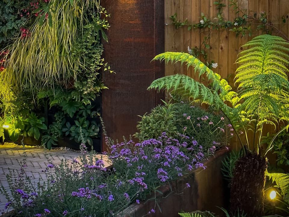 raised garden beds with purple verbena flowers in a garden illuminated at night