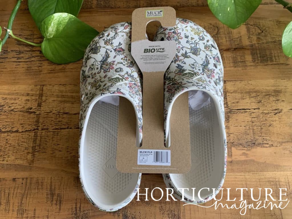 a pair of woman's white floral printed croc-style shoes on a table next to a houseplant