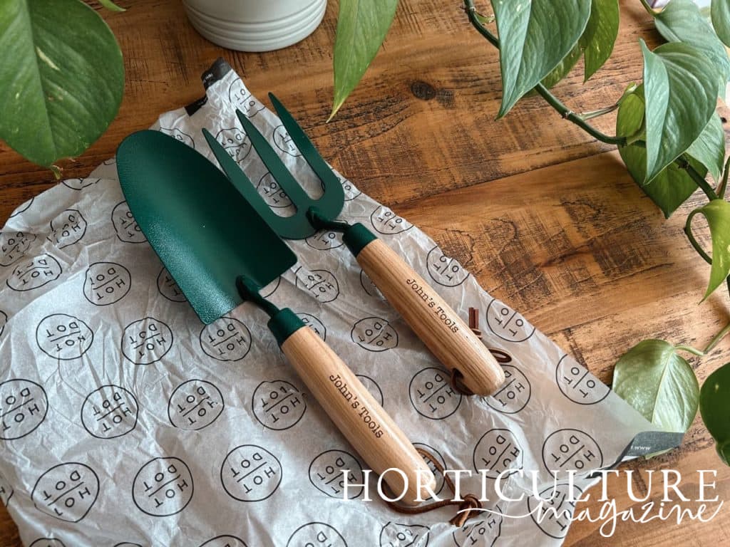 hand-held garden trowel and fork with personalisation on the handle reading 'john's tools' in its hot dot packaging