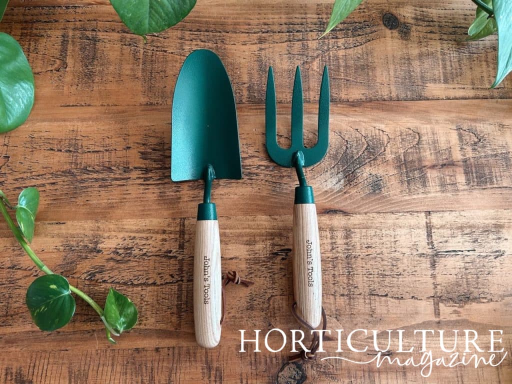green garden trowel and fork with wooden handles from Hot Dot Laser sat on a wooden surface