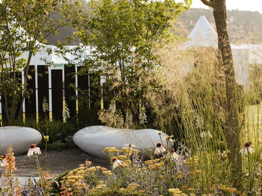 large stone seats in a garden surrounded by cream coloured ornamental grasses and orange flowering yarrow