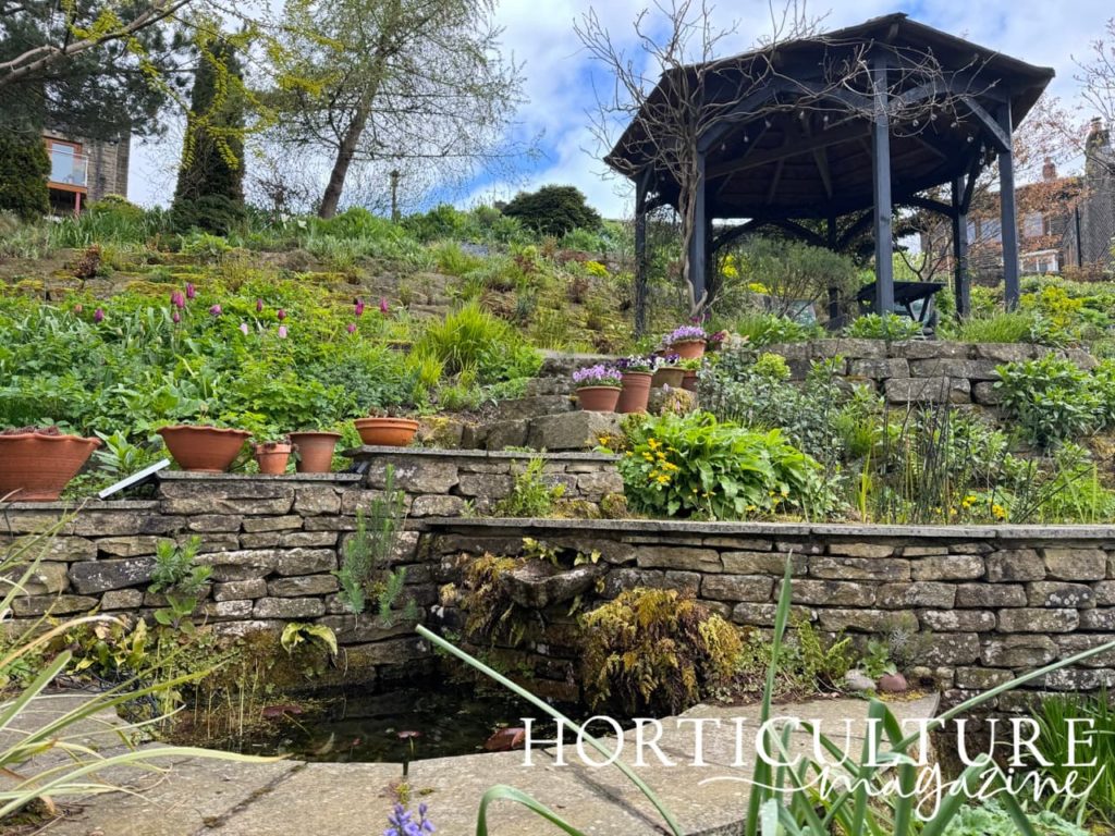 terracotta pots with plants in placed along a brick wall leading to a gazebo