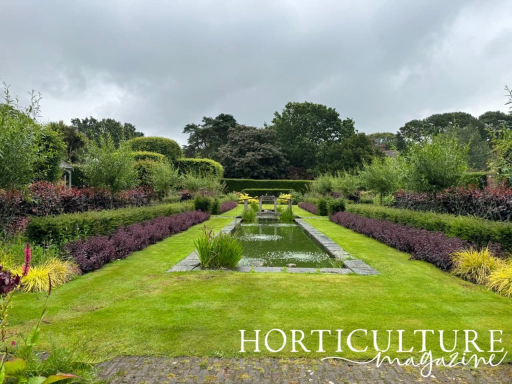 the pool garden at Abbeywood Estate with red and green foliage shrubs and trees growing around the edge